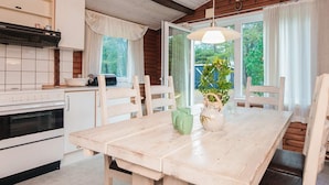 A kitchen with a stove, cabinets, and a window. There is a dining table with chairs and a vase with flowers. - 4 Star Holiday Home in Blavand (Blavand)