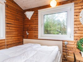 Une pièce de style cabane en bois, avec un lit, une fenêtre donnant sur les arbres et un luminaire fixé au mur.