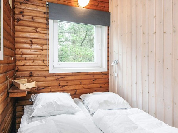 A wooden cabin room with a bed, a window, and a wall-mounted shelf. - 4 Star Holiday Home in Blavand (Blavand)