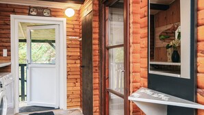 A log cabin with a wooden door, a small porch, a washing machine, and a mirror with a vase of flowers. - 4 Star Holiday Home in Blavand (Blavand)