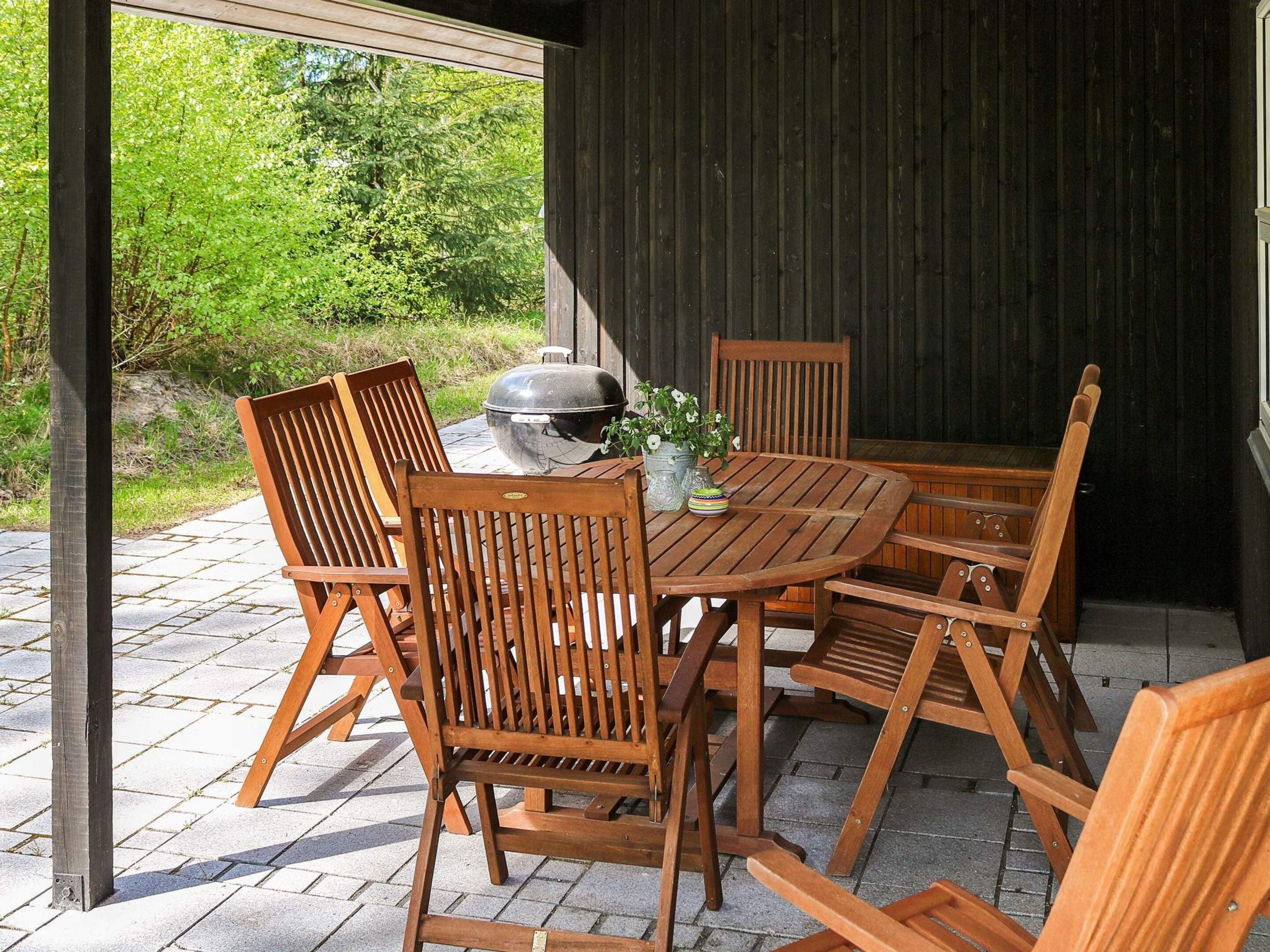 An outdoor wooden table with chairs, a grill, and potted plants.