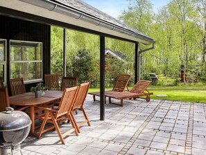 An outdoor patio with a table and chairs, a grill, and a covered seating area with a view of a garden. - 5 Star Holiday Home in Hadsund (Hadsund)