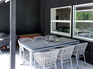 Une terrasse extérieure avec une table et des chaises, un barbecue et une fenêtre donnant sur un paysage verdoyant.