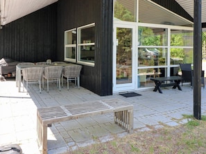 An outdoor patio with a barbecue grill, a table with chairs, and a wooden bench.