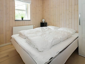 Une chambre à coucher avec un lit, une fenêtre, un radiateur et une table de chevet avec une lampe.