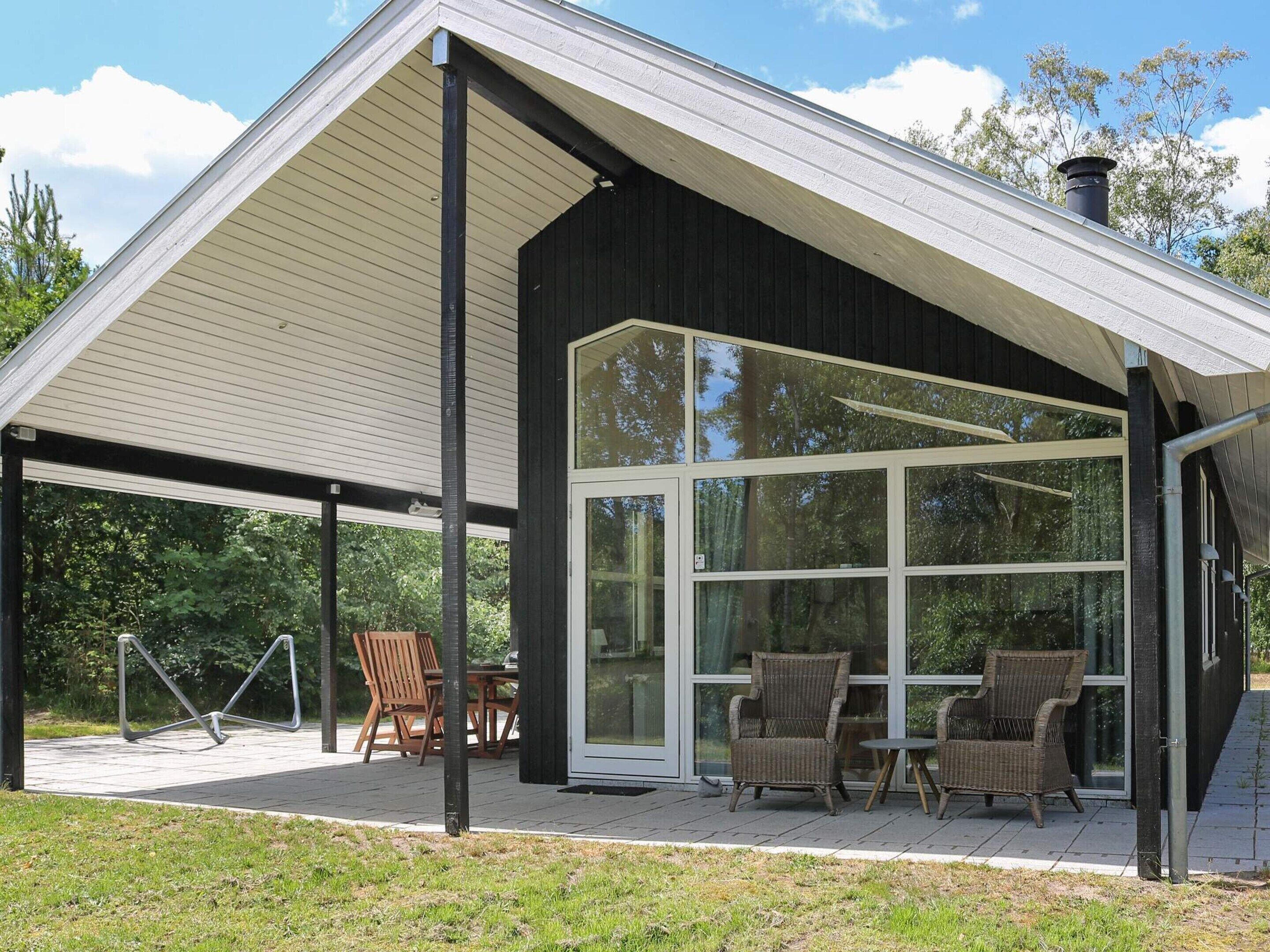 A covered outdoor seating area with chairs and tables, a large glass door, and a black exterior wall.