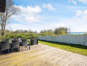 A wooden deck with outdoor furniture, a view of the sea, and a white fence. - Luxurious Holiday Home in Jutland with Hot Tub (Aabenraa)