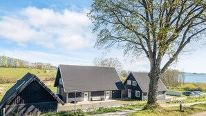 Una hilera de casas tradicionales de madera con techos inclinados, un camino pavimentado y un gran árbol en primer plano.