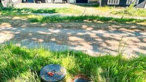 Un espacio al aire libre con césped, un objeto circular que podría ser un pozo o una fuente de agua, y un edificio al fondo.