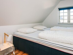 Una camera da letto con un letto singolo, biancheria bianca, un comodino con una lampada e una finestra con tende.