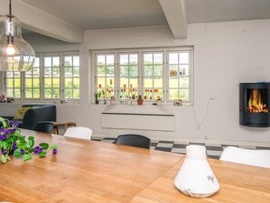 A modern kitchen with a large wooden table, white chairs, a hanging light fixture, and a built-in fireplace. - Luxurious Holiday Home in Jutland with Hot Tub (Aabenraa)