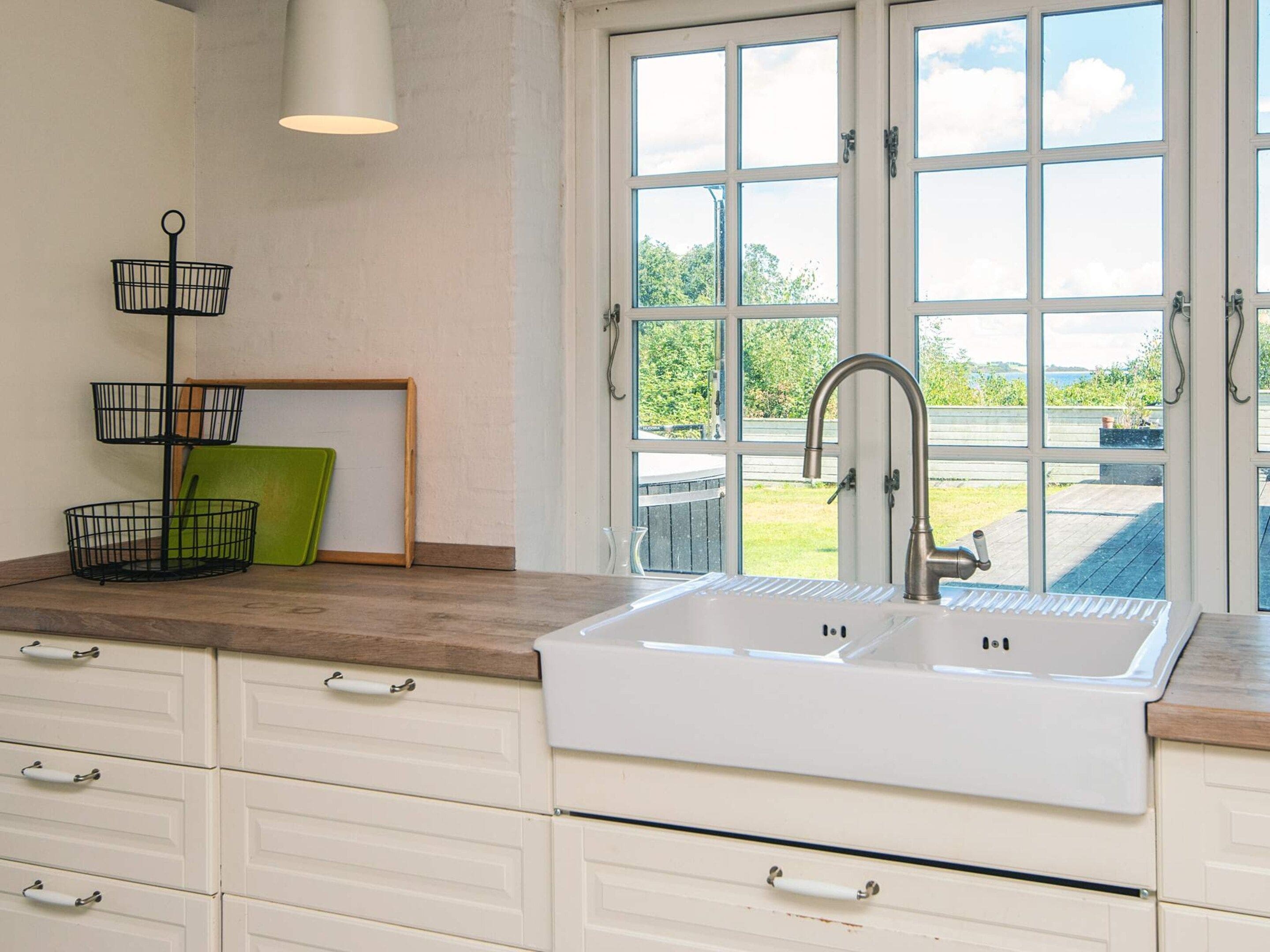 A kitchen with a white sink, wooden countertop, and a view of a garden through a large window.