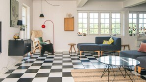 Una sala de estar con piso a cuadros, un sofá, una silla, una mesita redonda y una lámpara.
