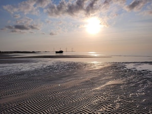 Ein Strand mit Wellen im Sand, ein Boot und Windkraftanlagen in der Ferne.