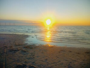 A beach with the sun setting over the water, creating a calm atmosphere.
