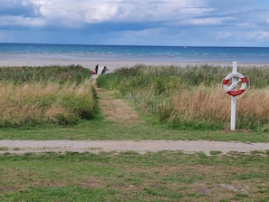 Ein Strandweg führt zum Meer, mit einem Rettungsbojen-Schild.