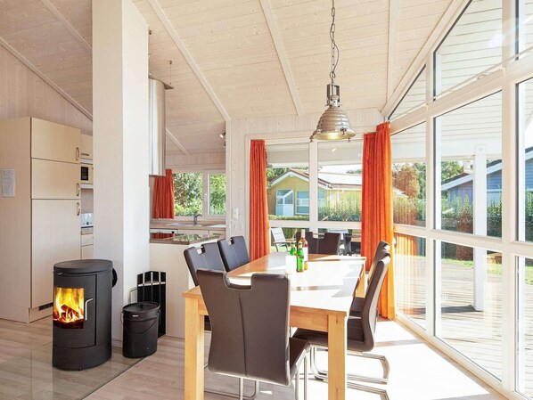 A modern kitchen with a wood-burning stove, a dining area with a table and chairs, and large windows offering a view of the outdoors. - Holiday Home in GrÃ¶mmitz (Groemitz)