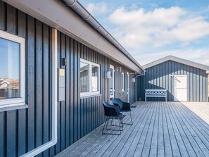 En bygning med træterrasse, flere vinduer og en hvid dør.