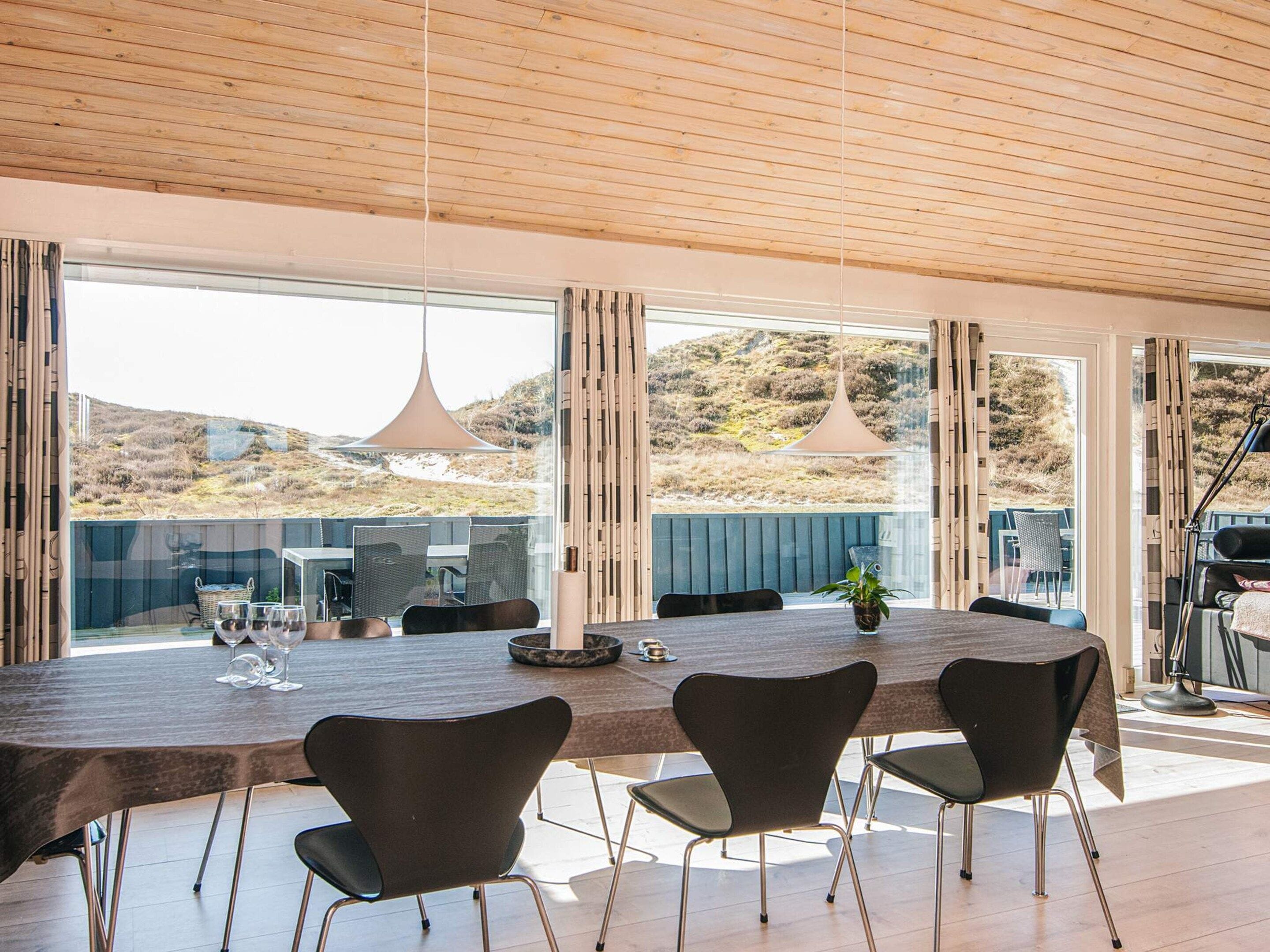A modern dining area with a large table, chairs, and a view of the outdoors.