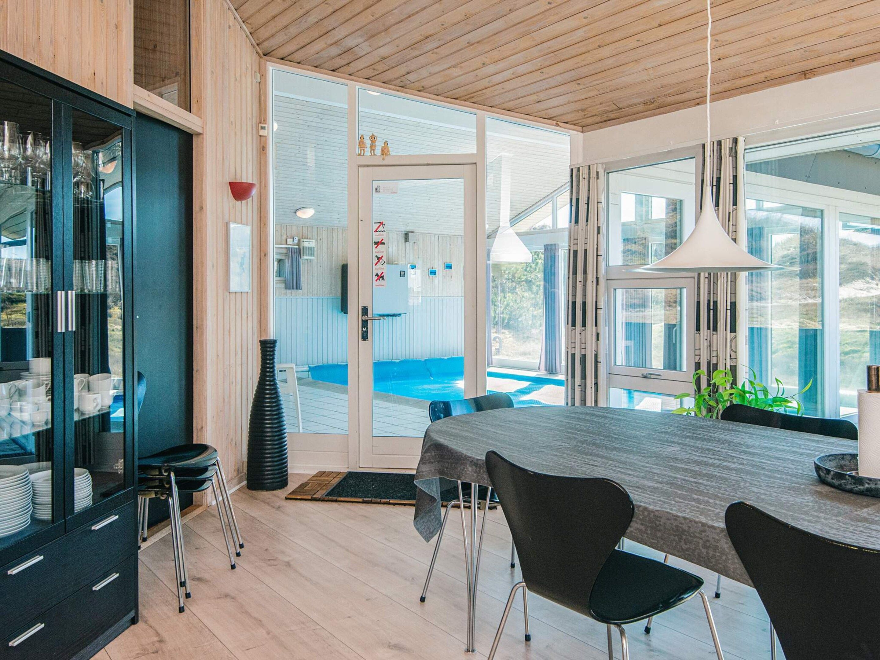 A modern kitchen with a large wooden table, black chairs, and a view of a swimming pool.