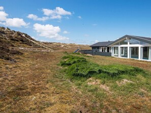 Une maison moderne dotée d’une grande façade en verre, située sur une colline verdoyante sous un ciel dégagé.