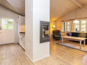 A room with a wooden floor, a white door, a kitchen area with cabinets, a dining table, a sofa, and a chair.