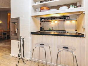 A compact kitchen with a black countertop, two bar stools, and a wooden wall. - 6 Person Holiday Home in Albaek (Aalbaek)