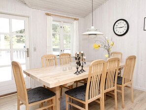 A dining room with a wooden table and chairs, a wall clock, and a hanging light fixture. - 6 Person Holiday Home in Albaek (Aalbaek)