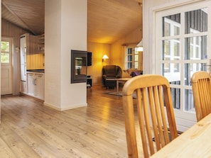 A room with wooden flooring, a dining table, chairs, a television mounted on the wall, and a window with curtains.