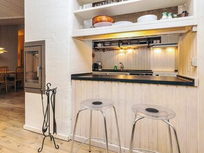 A compact kitchen with a black countertop, two bar stools, and a wooden wall.