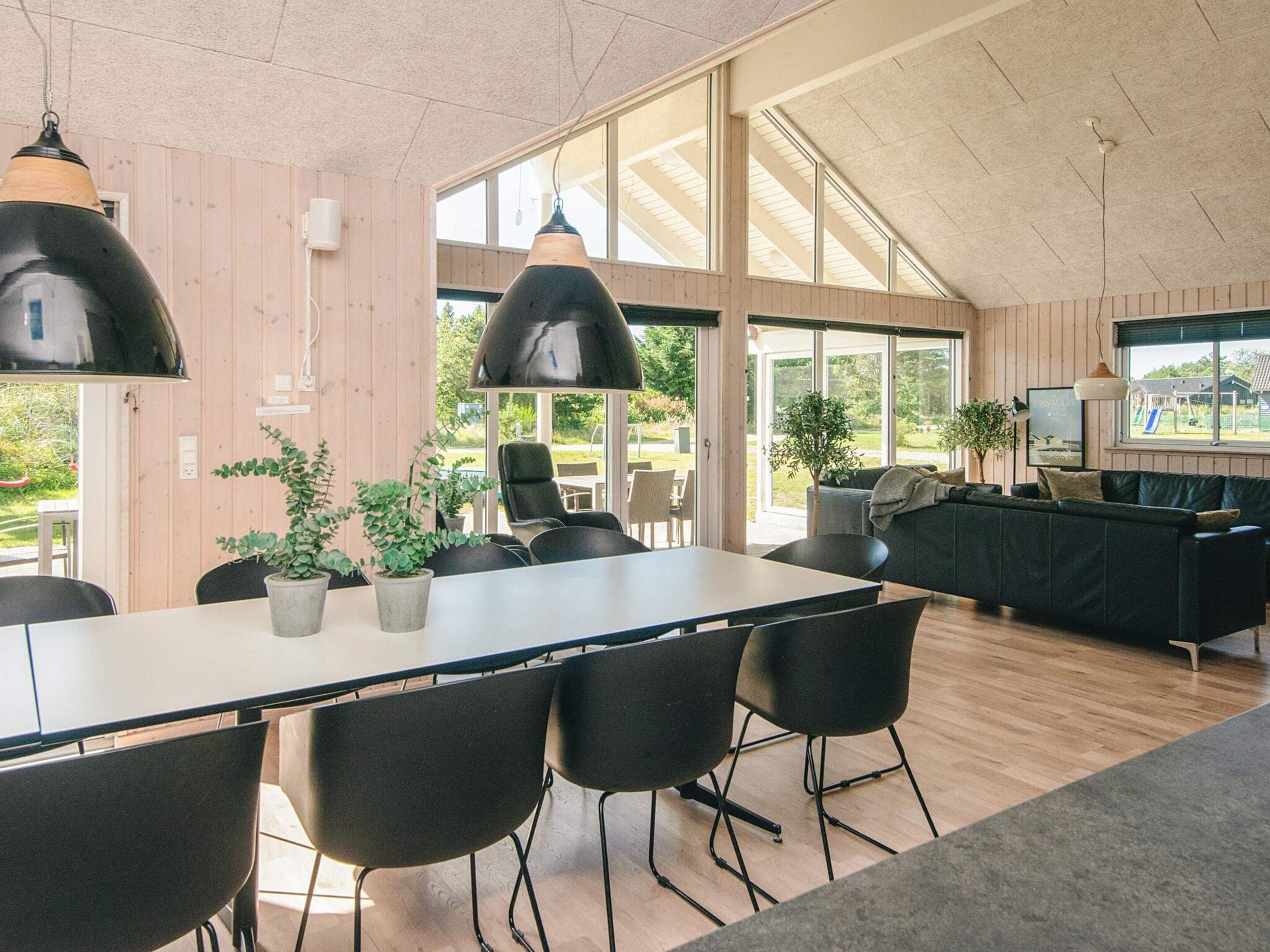 Een moderne keuken met een eetgedeelte, met een grote tafel, stoelen, hanglampen en uitzicht op het omliggende landschap.