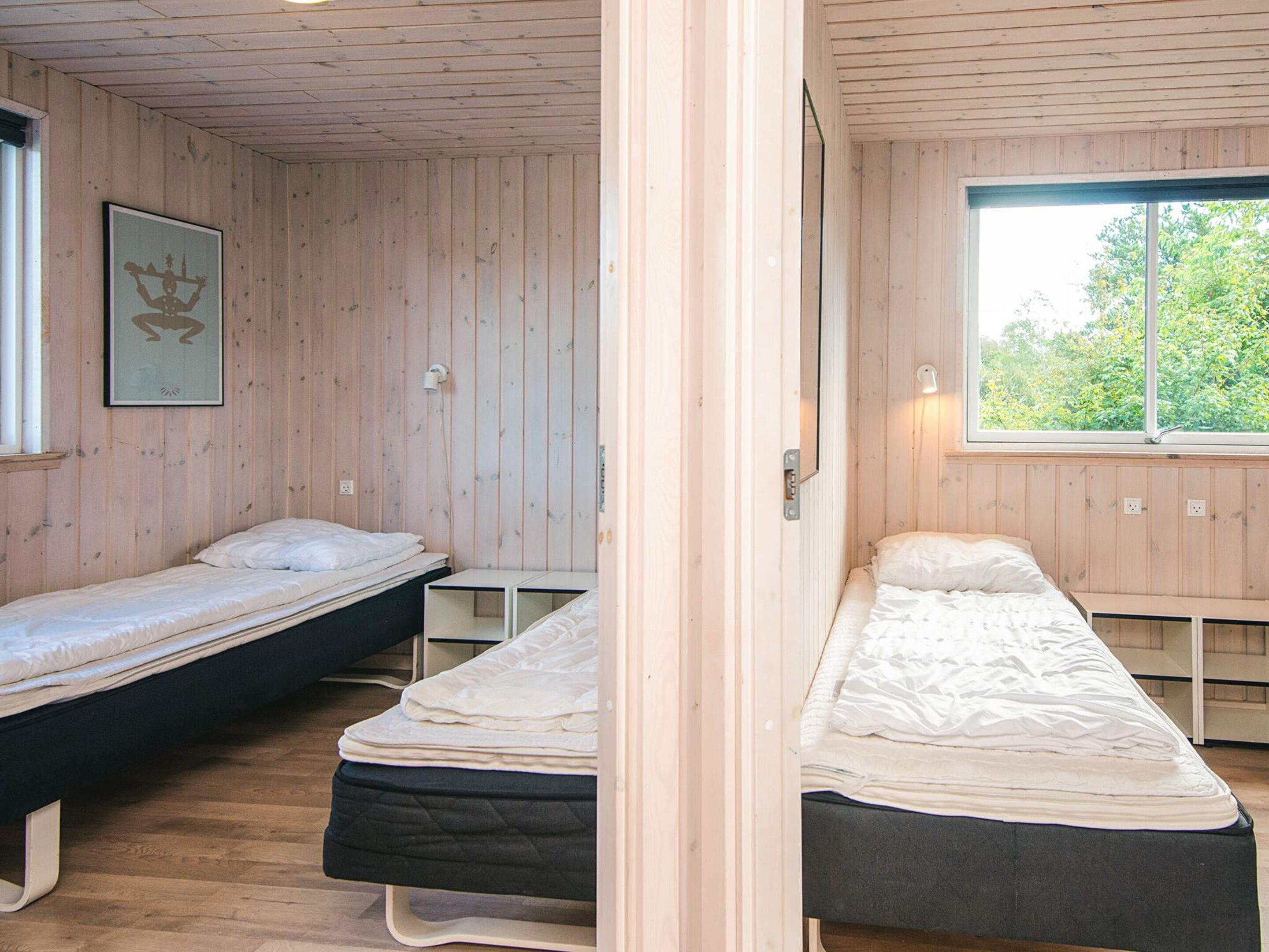 A room with two single beds, a wooden ceiling, a framed picture on the wall, and a window with a view of greenery.