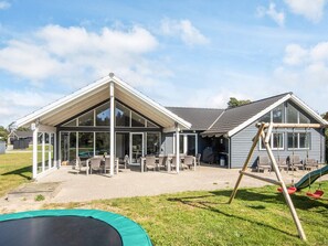 A modern house with a covered patio, outdoor seating, and a swing set.