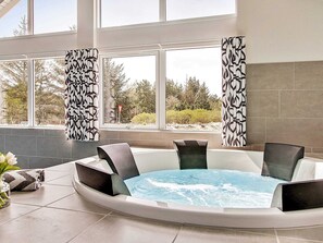 A spa area with a hot tub, large windows, and a view of trees and a road. - 5 Star Holiday Home in Blavand (Blavand)
