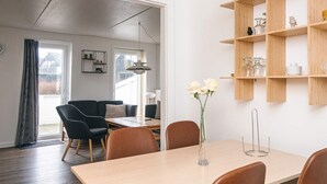 A modern living room with a sofa, dining table, and chairs. There is a vase with flowers on the table. - 6 Person Holiday Home in Romo (Rømø)