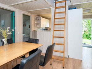 A modern interior with a wooden dining table, black chairs, a wooden ladder, and a kitchen area with cabinets and a countertop. - 12 Person Holiday Home in Nordborg (Nordborg)