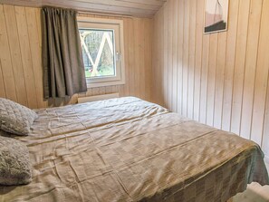 A room with wooden walls, a bed with a beige bedspread, a window with a view of trees, and a small picture on the wall. - 12 Person Holiday Home in Nordborg (Nordborg)