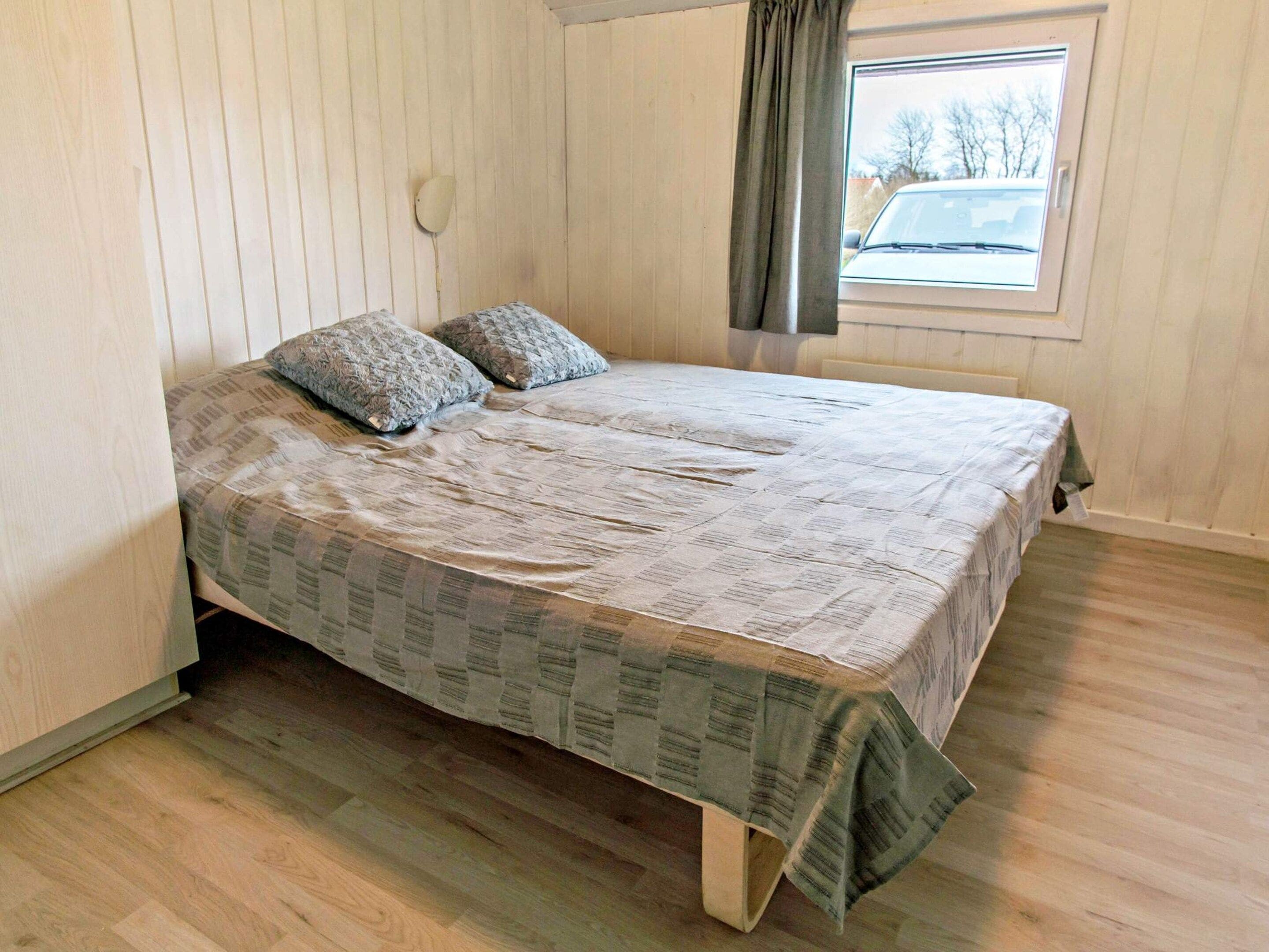 A single-bed room with a wooden floor, a window with a view of a car outside, and a curtain.