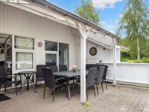 An outdoor patio with a table and chairs, a dartboard, and a white building with windows. - 12 Person Holiday Home in Nordborg (Nordborg)