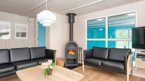 Ein modernes Wohnzimmer mit zwei schwarzen Ledersofas, einem Holztisch mit Blumenvase, einem schwarzen Kaminofen und einem großen Fenster mit blau getöntem Glas.