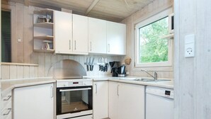 Eine kompakte Küche mit weißen Schränken, einem Backofen, einem Spülbecken und einem Fenster mit Blick auf Grünflächen.
