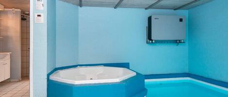 A swimming pool area with a hot tub, tiled flooring, and a ceiling with visible beams.