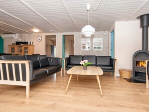 A modern living room with a black leather sofa, a wooden coffee table with a vase, and a wood-burning stove. - 12 Person Holiday Home in Nordborg (Nordborg)