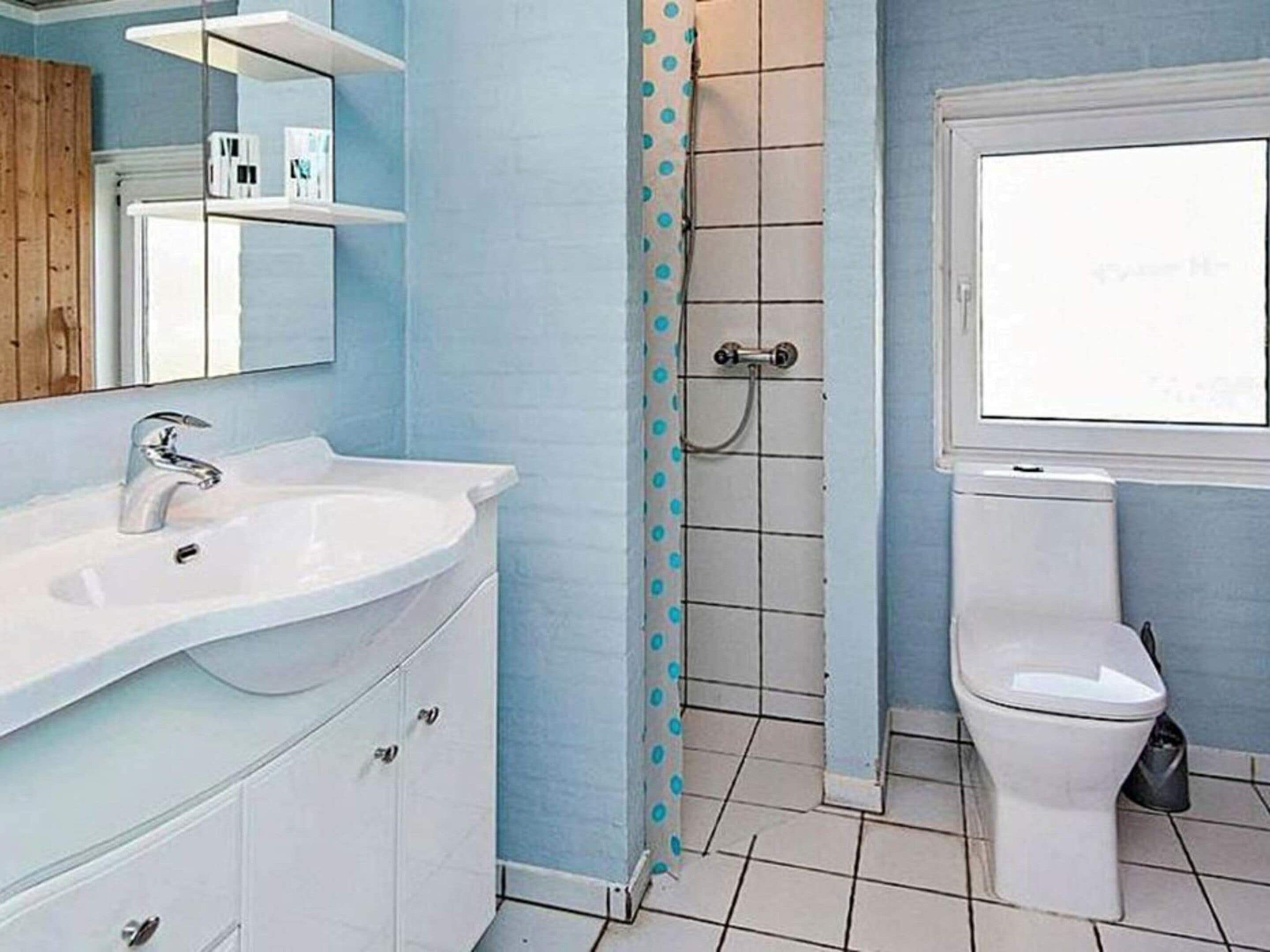 Ett badrum med ett vitt handfat, en toalett, en dusch med en blå duschdraperi och en spegel ovanför handfatet.