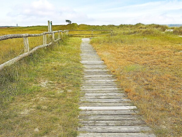 A wooden boardwalk leading through a grassy field with a fence on one side and a hill in the distance.