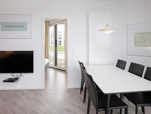 A modern hotel room with a large flat-screen TV, a dining table with chairs, a hanging pendant light, and a framed map on the wall. - Holiday Home in Wendtorf (Schönberg)