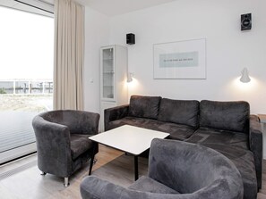 Ein modernes Wohnzimmer mit einem grauen Sofa, zwei Sesseln, einem kleinen weißen Tisch und einer Glasschrank.