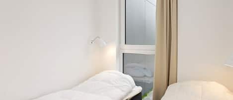 Habitación pequeña con cama individual, ventana y lámpara en la pared.