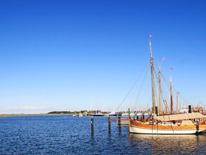 A docked boat with multiple masts and flags, surrounded by calm water and other boats in the background. - Holiday Home in Wendtorf (Schönberg)