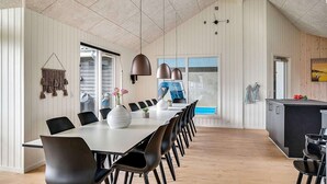 Un comedor moderno con una mesa larga, sillas negras e iluminación colgante.